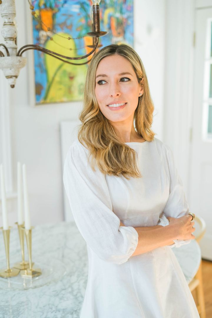 Tamara Ashworth in a white dress with her arms crossed, smiling and looking away from the camera.