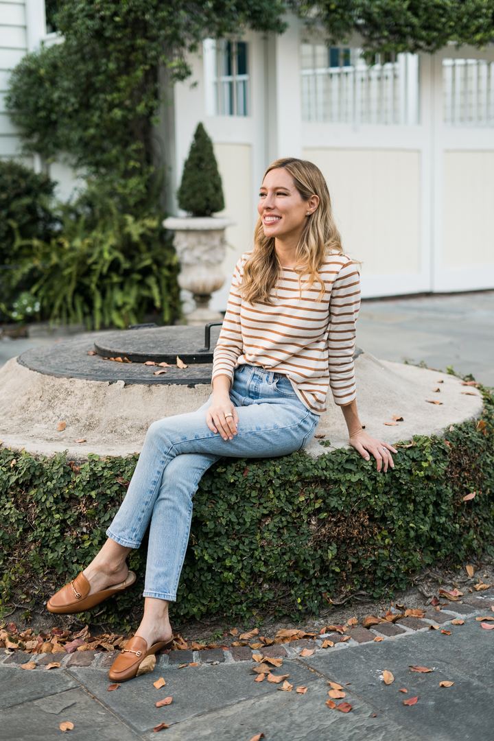 Tamara Ashworth sitting on a garden wall in Charleston and laughing, looking off to the side.