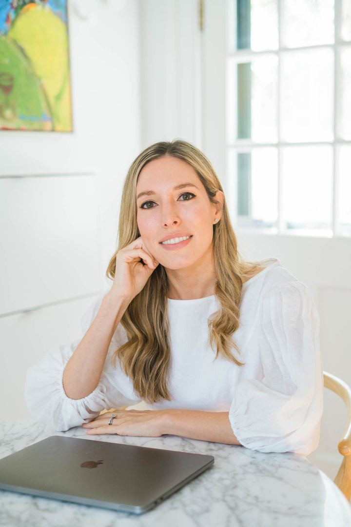 Tamara Ashworth seated at a marble table with her chin resting on her hand and a closed laptop in front of her.